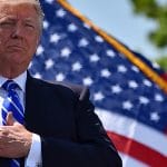 Der US-Präsident legt bei der Abschlussfeier der Küstenwachen-Akademie vor einer US-Flagge die Hand auf die Brust; rechts daneben ein Offizier in weißer Uniformmütze.