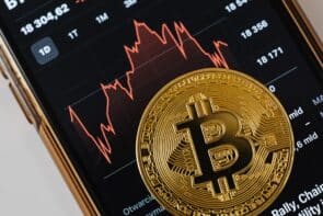 Foto eines physischen Bitcoins auf einer Handy-App, die Crypto-Kurse anzeigt