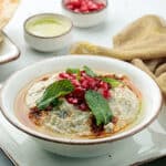 Tipps & Tricks: Mutabal – das Beste aus der Aubergine Mutabbal – das Wort kommt vom arabischen „tabbala“, was „würzen“ bedeutet, und genau das macht man mit diesem Gericht. (MEMO). Eines der Dinge, auf die ich mich im Sommer am meisten freue, sind Grillabende. Ich liebe alles, was über dem Feuer gegrillt wird, sowie den rauchigen Geschmack, den das Essen dadurch bekommt. Von Maha Salah Wenn ich also im Winter Lust auf etwas Räucheriges habe, lege ich ein paar Auberginen auf den Herd und mache einen meiner Lieblingsdips, Mutabbal. Beliebte Variante von Mutabal Die beliebteste Variante von Mutabbal wird mit feuergerösteten Auberginen zubereitet. Aber auch viele andere saisonale Gemüsesorten wie Kürbis, Butternusskürbis oder Zucchini werden verwendet. So unterschiedlich die Gemüsesorten auch sein mögen, die Zutaten, also die Gewürze, sind im Wesentlichen die gleichen: Tahini, Knoblauch, Zitronensaft und Olivenöl. Einige Leute, darunter ich, fügen unserem Mutabbal gerne Joghurt hinzu, weil es ihm eine samtige Konsistenz verleiht. Manchmal, wenn ich in der Stimmung für etwas Schärfe bin, füge ich ein wenig gehackte Chilischote hinzu. Ich empfehle, die Auberginen auf offener Flamme zu rösten, weil das den besten Rauchgeschmack ergibt und sehr schnell geht. Sie können die Auberginen aber auch in Folie einwickeln und im Ofen garen. Wenn Sie das getan haben, müssen Sie nur noch die restlichen Zutaten untermischen und genießen! Ich empfehle, die Zutaten unterzumischen, solange die Auberginen noch warm sind, weil sie sich dann besser vermischen und alles so aromatisch wird. Ich lasse den Dip dann gerne 15-20 Minuten ziehen, damit sich die Aromen richtig vermischen. Die Schritte sind sehr einfach. Aber achten Sie darauf, dass Sie die bestmöglichen Zutaten verwenden, damit Ihr Mutabbal unwiderstehlich wird. Ich zerdrücke den Knoblauch gerne in einem Mörser und Stößel, anstatt gekaufte Knoblauchpaste zu verweden, da frischer Knoblauch in Dips viel besser schmeckt. Das von mir verwendete Mischungsverhältnis ist das, was ich bevorzuge, da ich mein Mutabbal eher würzig mag, aber für dieses Gericht ist es am besten, wenn Sie nach und nach die Zutaten in dem von Ihnen gewünschten Verhältnis hinzufügen. Wenn mein Mutabbal nach meinem Geschmack zubereitet ist und geruht hat, löffele ich ihn gerne mit heißem Fladenbrot oder selbstgemachten Pita-Chips und genieße den samtigen, würzigen Dip. Er passt auch hervorragend zu gegrilltem Fleisch, zu Huhn oder als Teil eines größeren Mezze-Tellers. Zutaten: 2 mittelgroße Auberginen 1-2 Teelöffel Knoblauchpaste (nach Geschmack) 1 Esslöffel Joghurt 1-1,5 Esslöffel Tahinpaste (nach Belieben) 2 Esslöffel Zitronensaft Salz und Pfeffer 1 Esslöffel Olivenöl, plus zusätzliches Olivenöl zum Beträufeln Legen Sie die gewaschenen und getrockneten Auberginen auf eine offene Flamme und wenden Sie sie regelmäßig, bis sie weich sind. Alternativ können Sie die Auberginen auch in Folie einwickeln und im Ofen weich backen. Platzieren Sie die gekochten Gemüse in eine Schüssel und decken Sie sie für 3-5 Minuten mit Plastikfolie ab. So löst sich die Haut und lässt sich leicht schälen. Die Auberginen öffnen und das Innere in die Schüssel schöpfen. Die Haut wegwerfen. Die Auberginen ein wenig pürieren und dann die restlichen Zutaten hinzufügen. Mischen Sie alles, bis es vollständig eingearbeitet ist, und schmecken Sie es ab. Den Geschmack anpassen und in eine Servierschüssel umfüllen. Großzügig mit Olivenöl beträufeln und mit dampfendem, heißem Fladenbrot genießen.